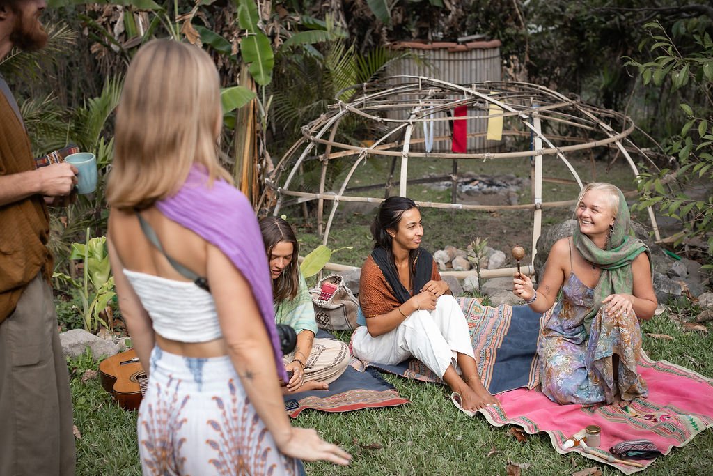 Women sitting on blankets beside a temazcal dome frame