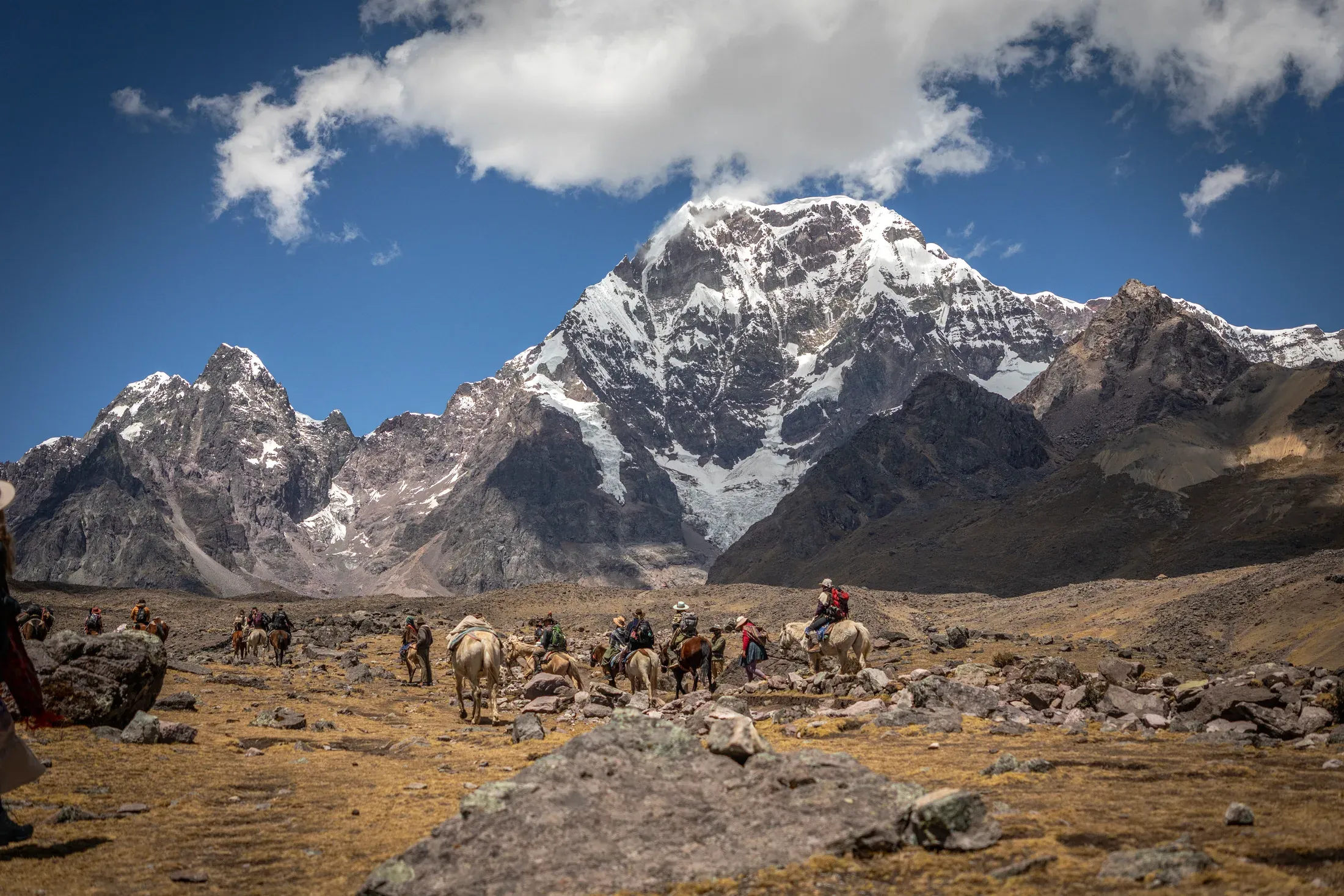 A caravan of pilgrims and horses crosses the high Andean plateau beneath a snow-covered peak