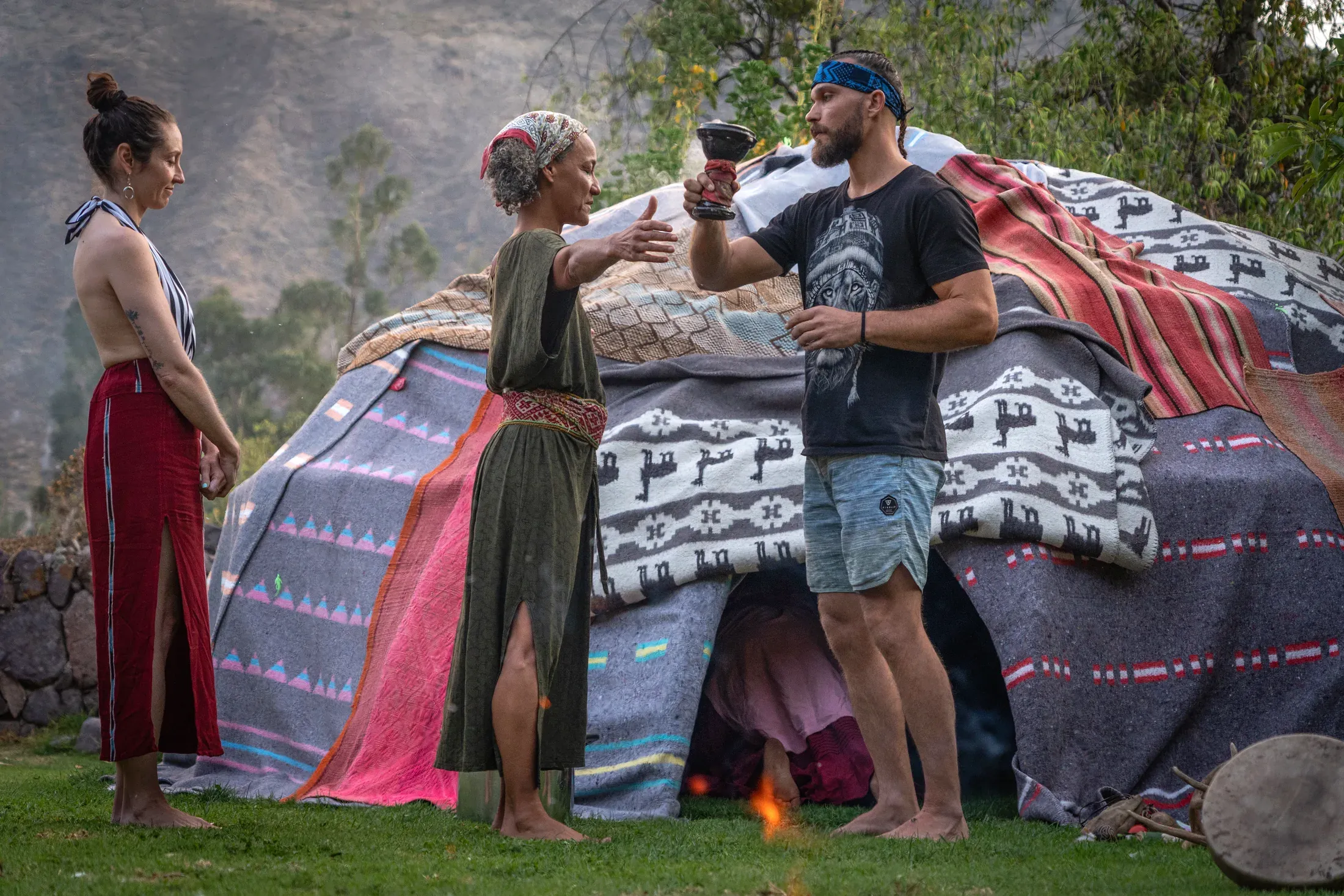 A woman blessing a man with smoke outside a blanket-covered sweat lodge