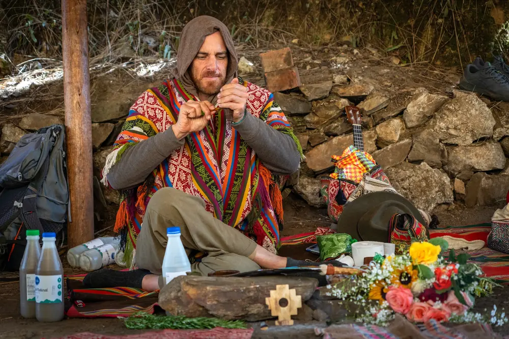 A man in a bright woven poncho prepares an offering beside an altar of flowers