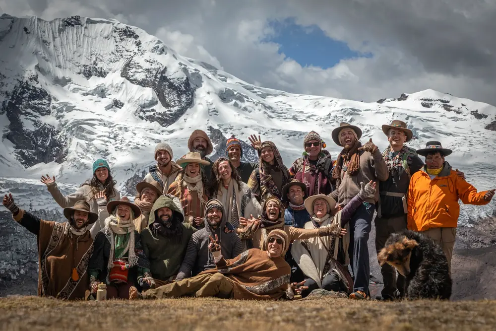 A joyful group of pilgrims with arms raised in front of a snow-covered mountain