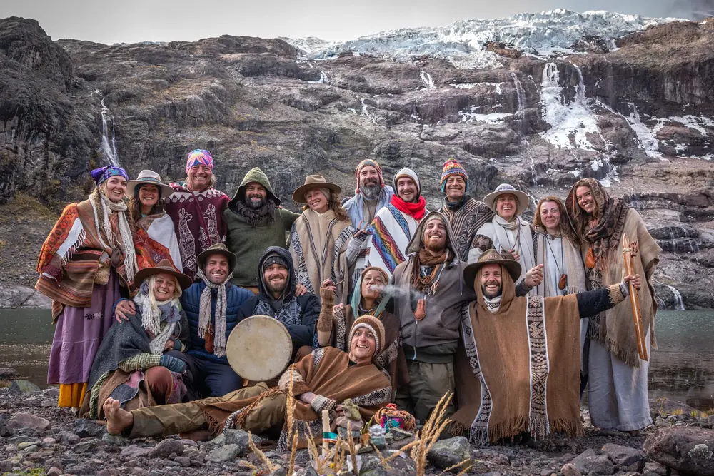 A group portrait of pilgrims in ponchos in front of a glacier and waterfall