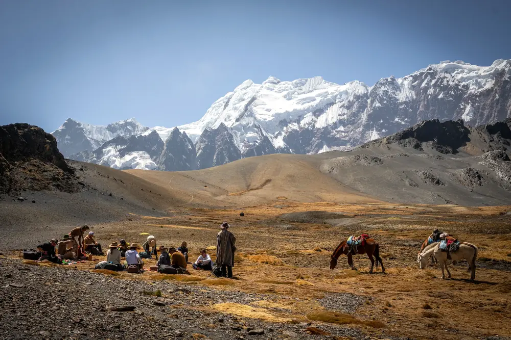 Pilgrims resting on the plateau with horses nearby and a snowy range in the distance
