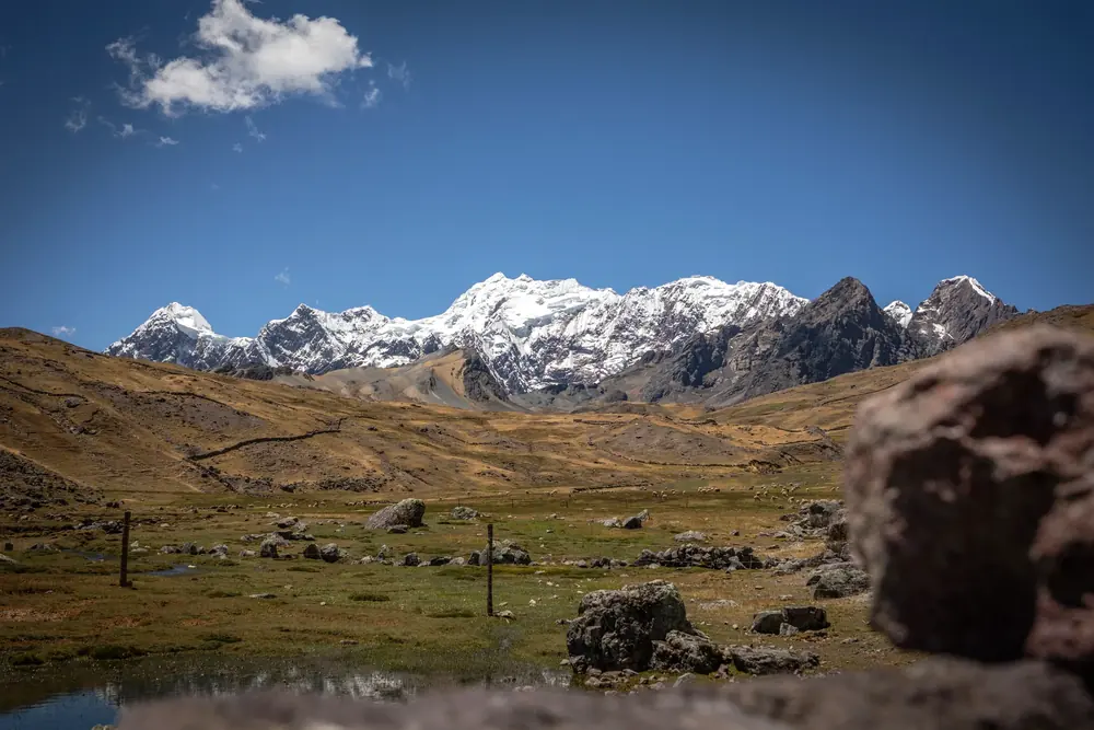 A high-altitude valley with a small lake and a line of snowy peaks