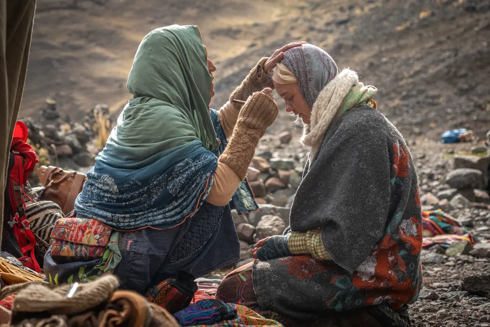 Two women in shawls share a quiet moment on the mountainside