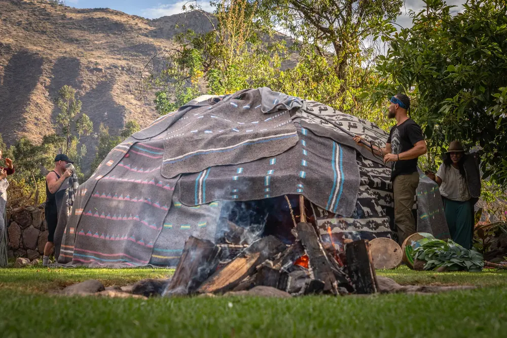 A sweat lodge draped in blankets with a fire burning beside it