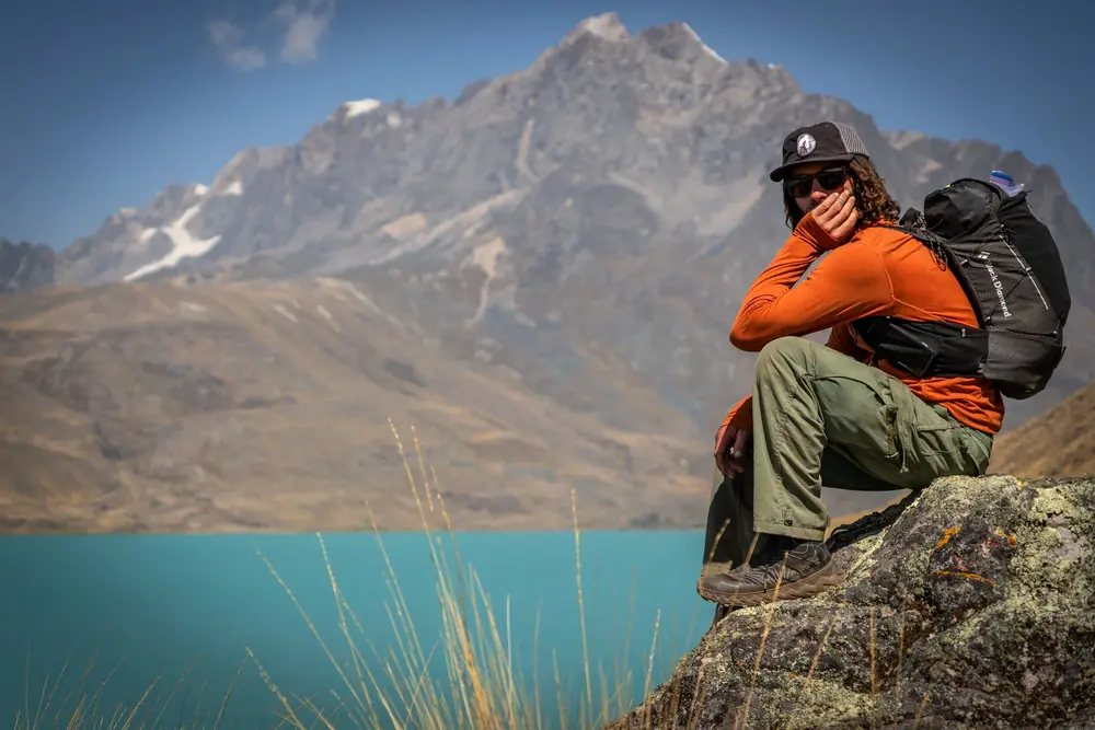 A hiker rests on a rock above a turquoise lake with a rugged peak behind