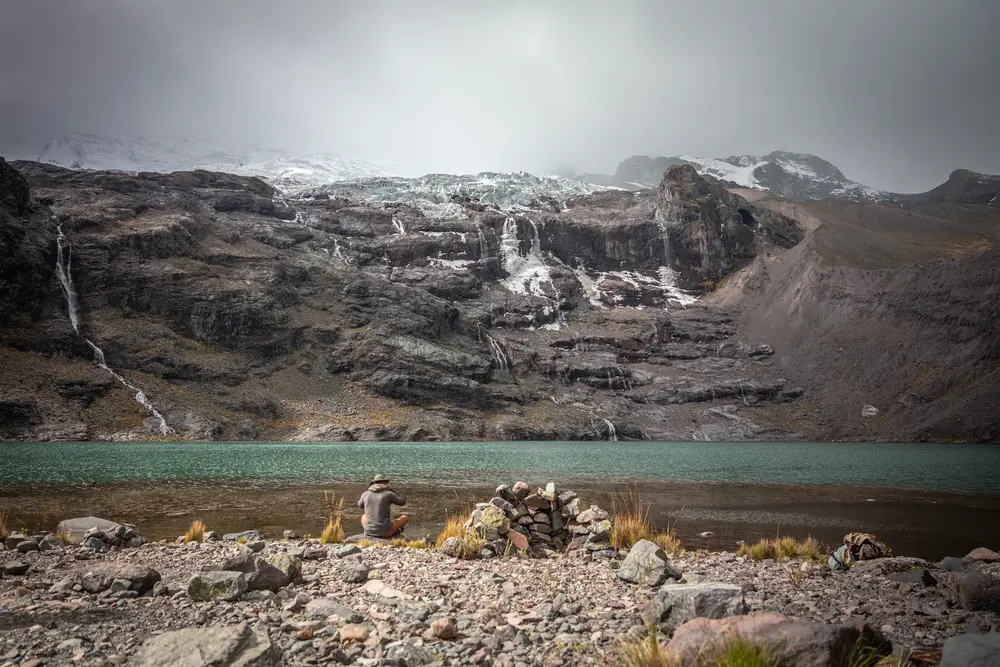 A waterfall above a mountain lagoon with a small stone cairn at the shore