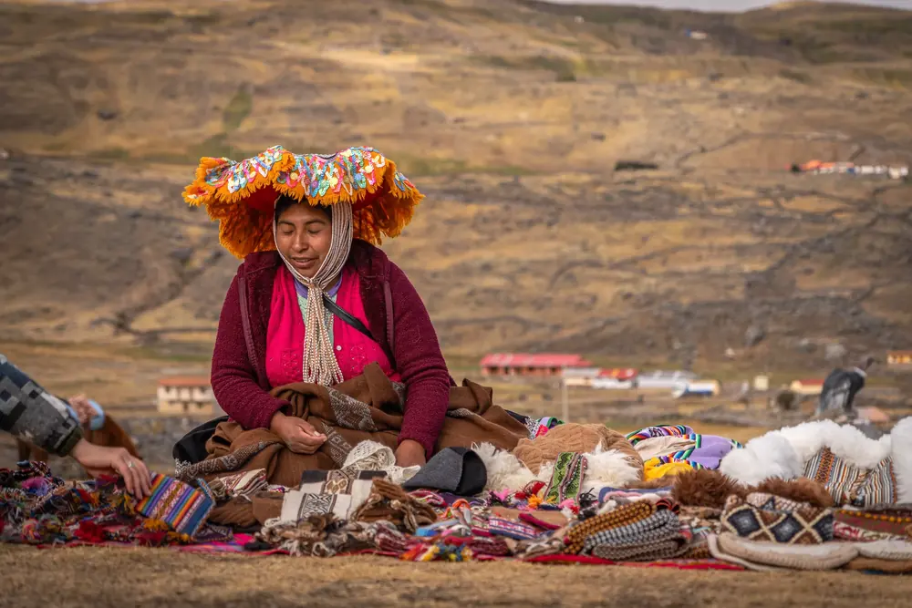 A woman in a flower-shaped hat displays handwoven textiles on the ground