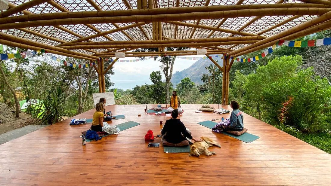 People sitting quietly on cushions on the open-air deck, with prayer flags overhead