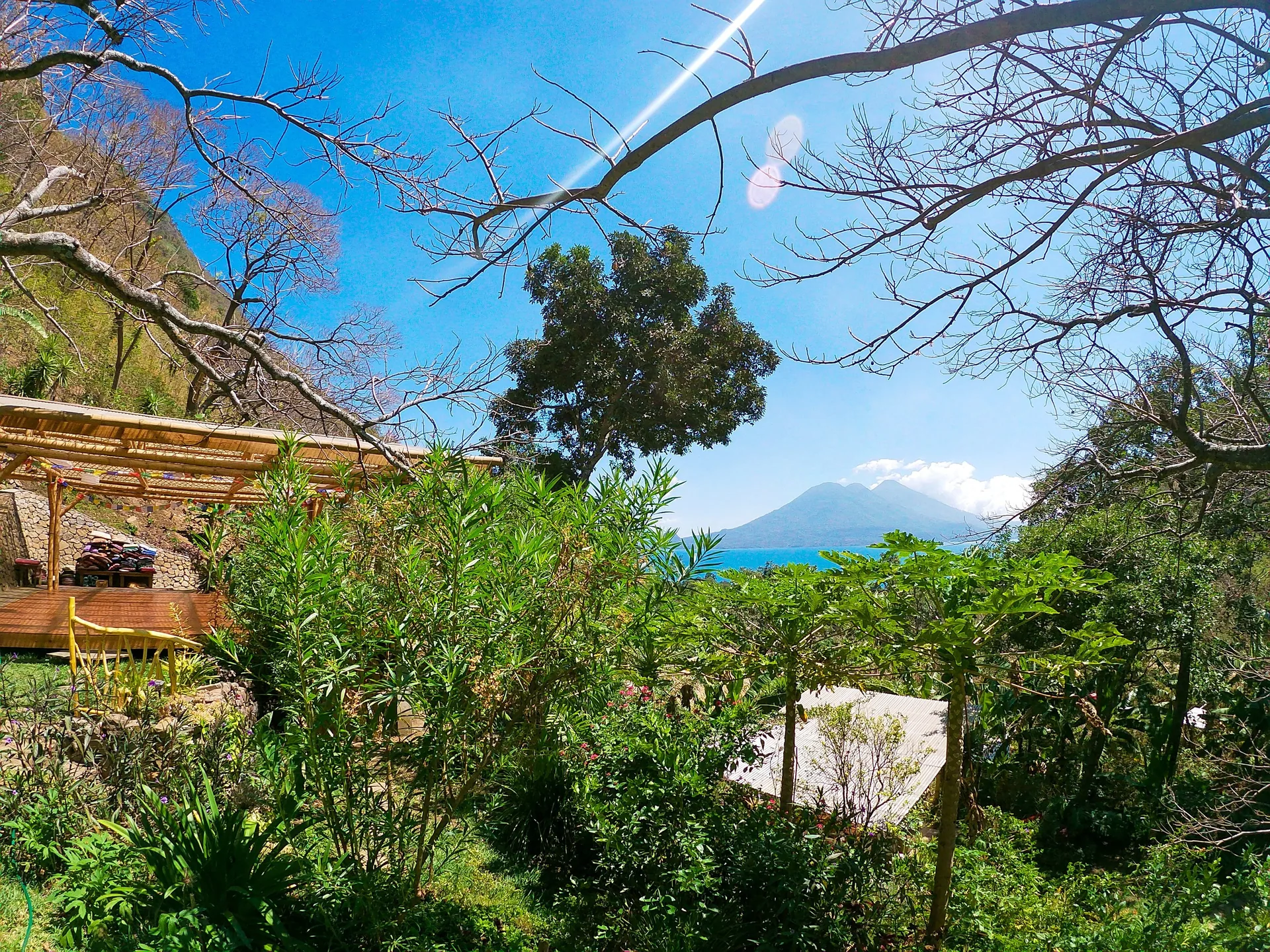 The gardens of Casa Kula on a sunny day, with the open-air deck among the trees and Lake Atitlán and a volcano beyond