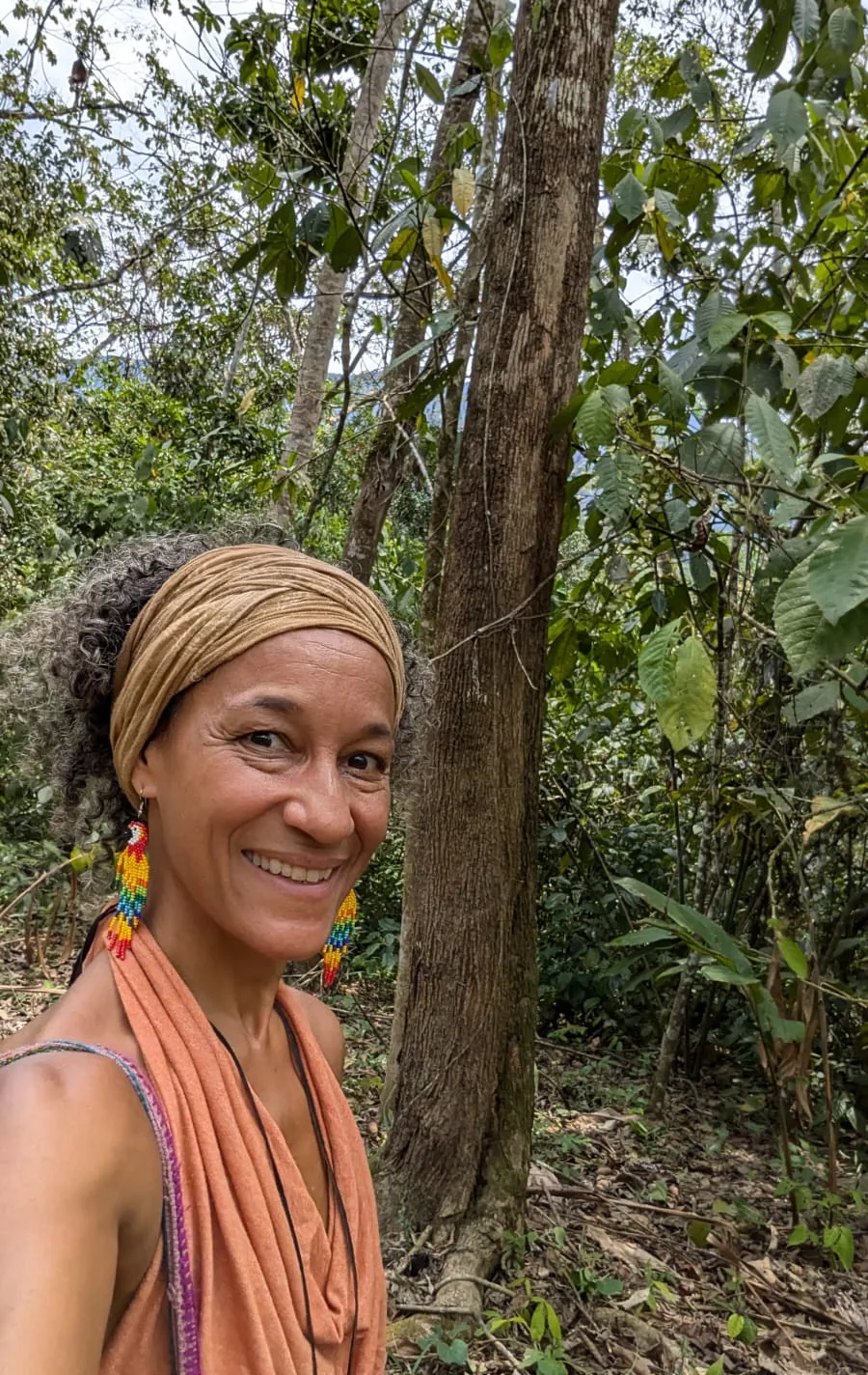 Ananda smiling among the trees, wearing a woven headwrap
