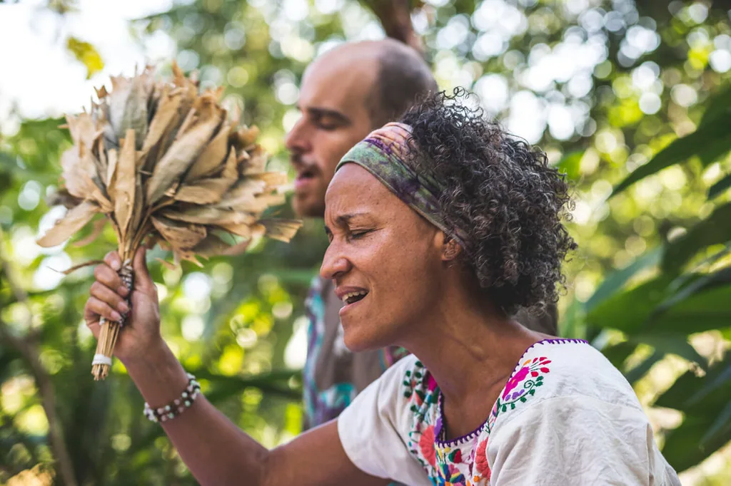 Ananda in ceremony holding a leaf rattle, with Coby behind her
